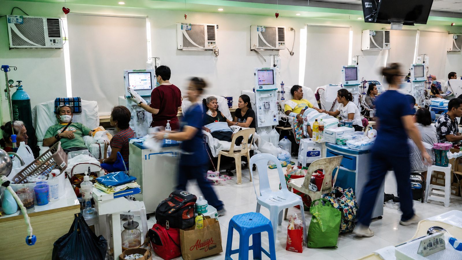 A busy dialysis floor during a treatment shift. Patients occupy every station while nursing staff move between them.